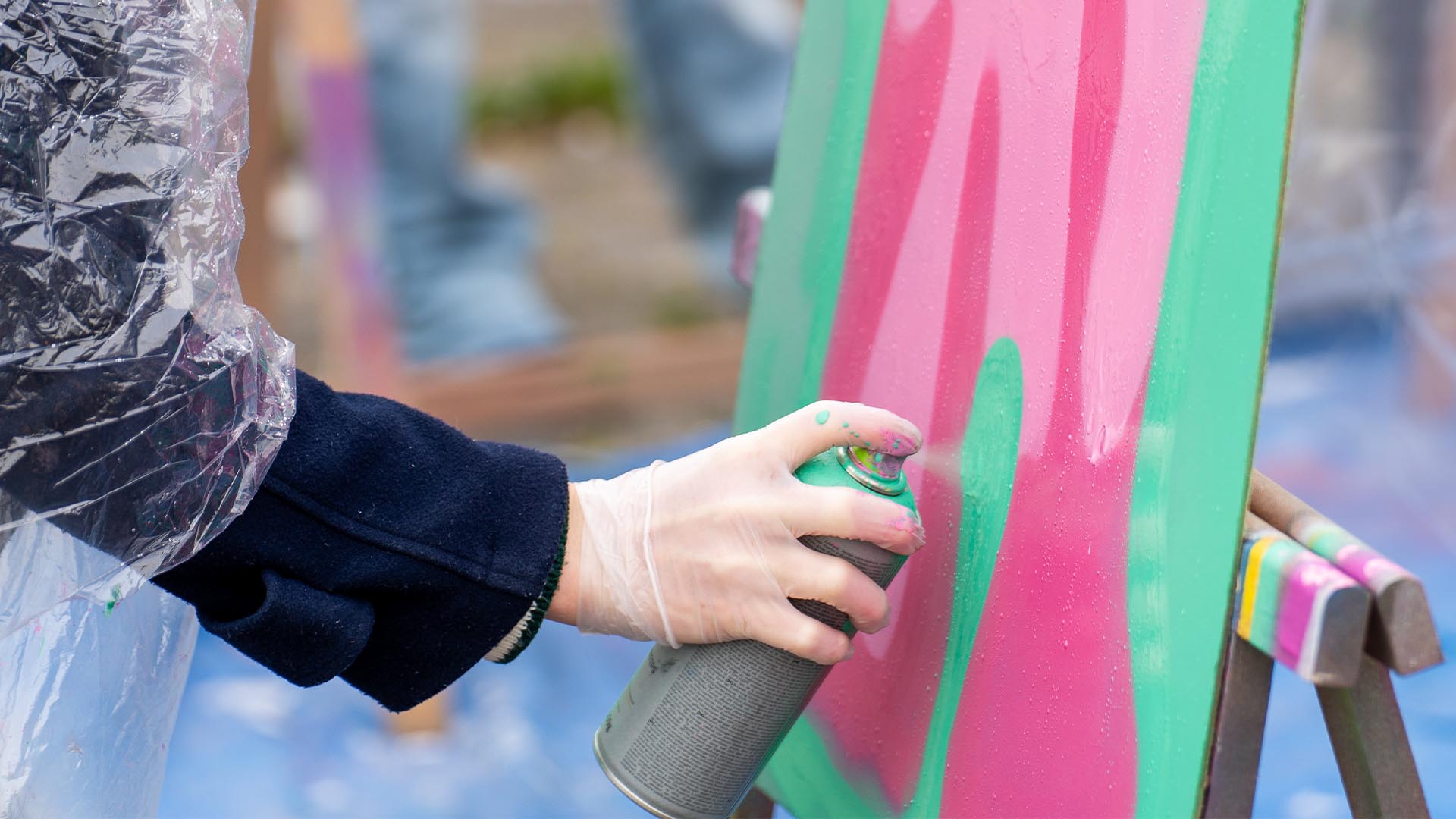 Deelnemer spuit graffiti op houten plaat tijdens Workshop Graffiti.