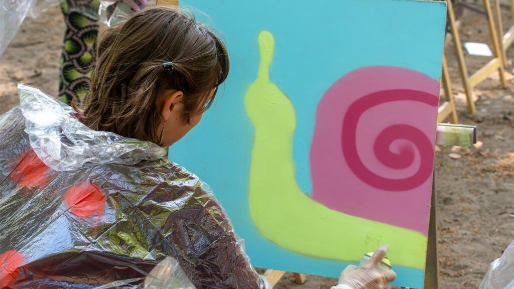 Deelneemster maakt met graffiti een slak tijdens de Workshop Graffiti.