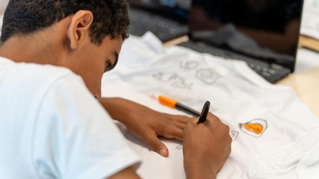 Leerling kleurt met textielstiften op t-shirt tijdens de Workshop T-Shirt Ontwerpen.