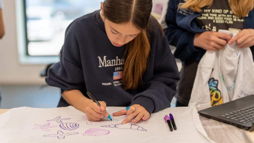 Deelnemer kleurt met verschillende textielstiften op het t-shirt tijdens de Workshop T-Shirt Ontwerpen.
