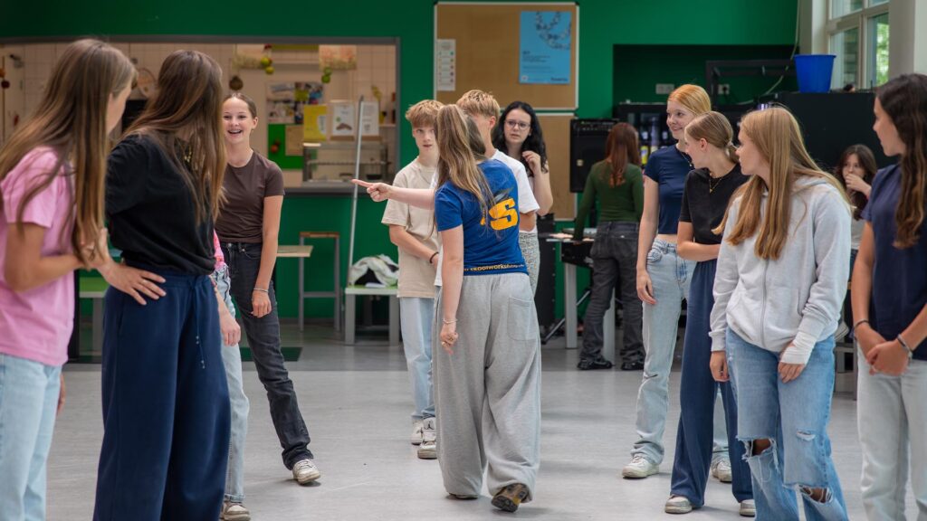 De workshopdocent doet een warming-up met de deelnemers en verdeelt hen in twee groepen tijdens de Workshop Breakdance.