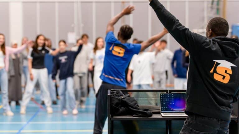 Groep leerlingen poseert met drumstokken samen met een begeleider