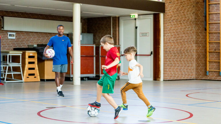 Leerlingen spelen pannavoetbal in een kooi tijdens een sportieve workshop op school.