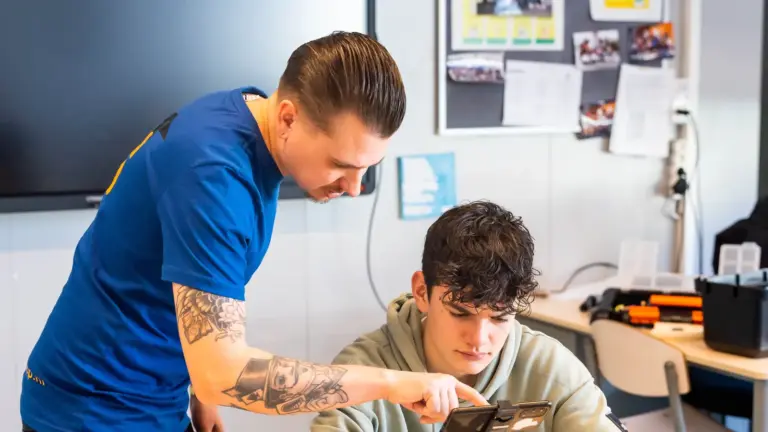 Workshopdocent helpt een leerling met filmen via een telefoon op statief
