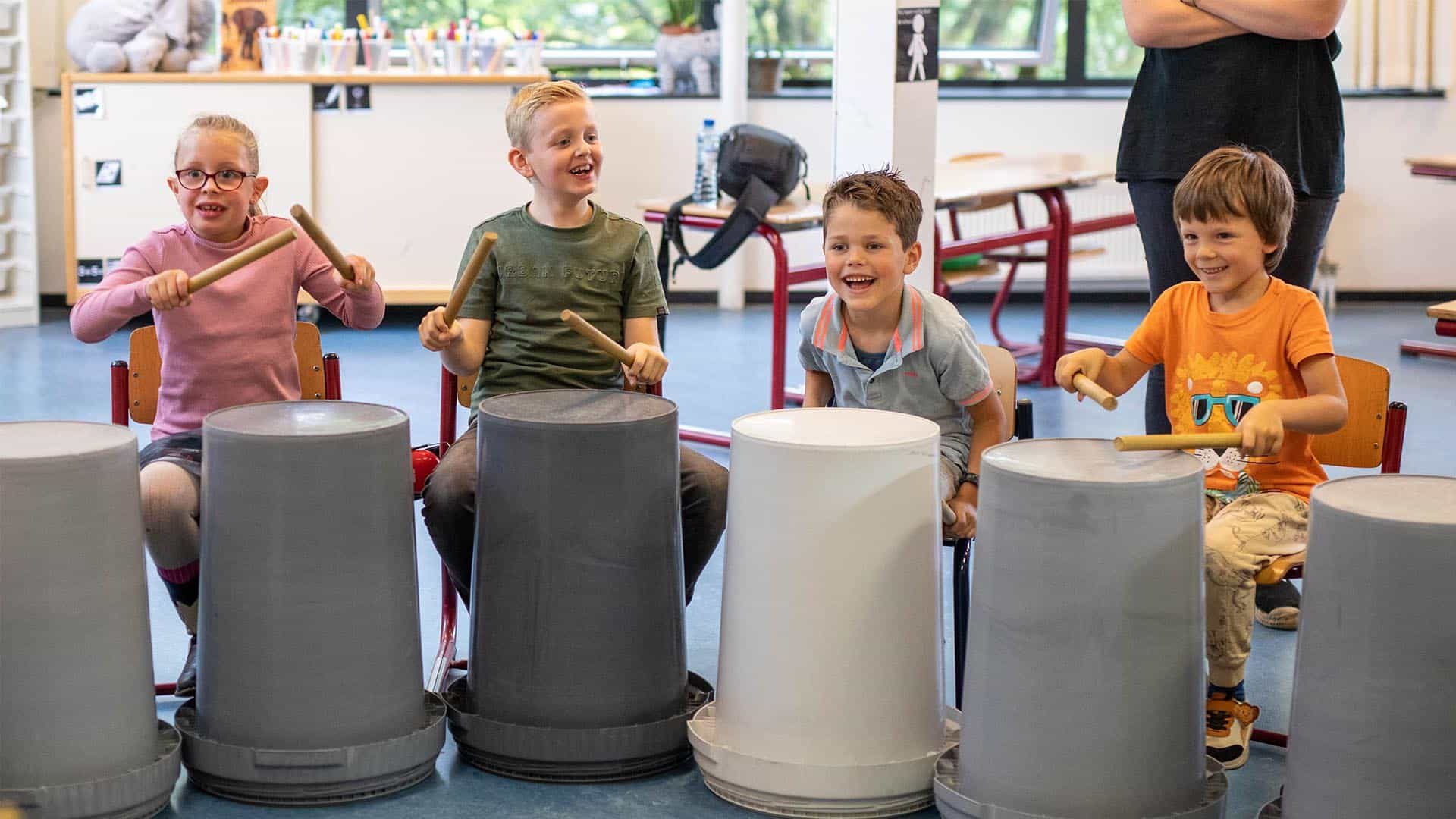 Kinderen van de BSO lachen tijdens de Workshop Ghetto Drums die wordt verzorgd door Skool Workshop als activiteit in de herfstvakantie.